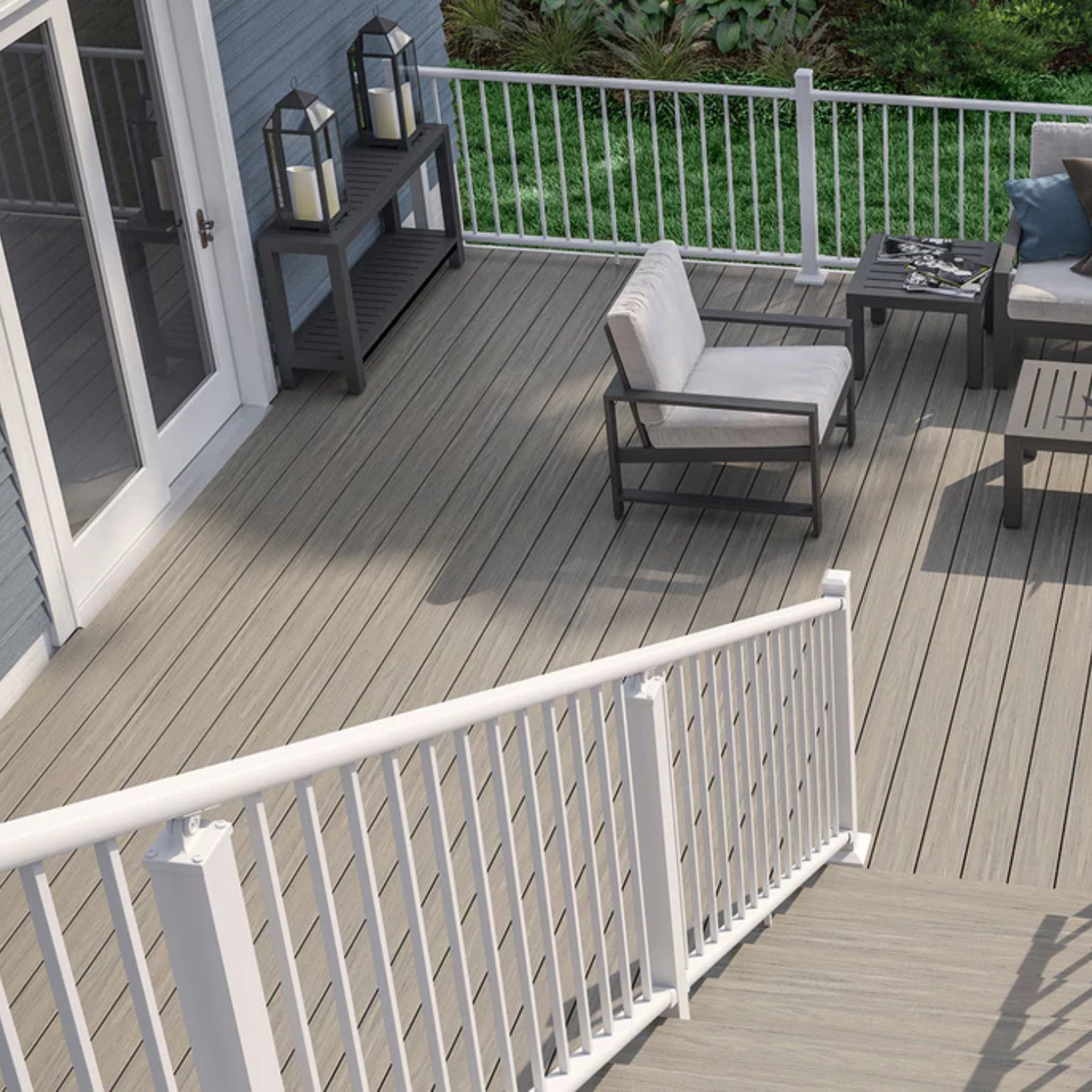 An elevated outdoor deck featuring Deckorators Venture Saltwater gray composite decking, white aluminum railing, and modern gray patio furniture, complementing the light blue house siding.