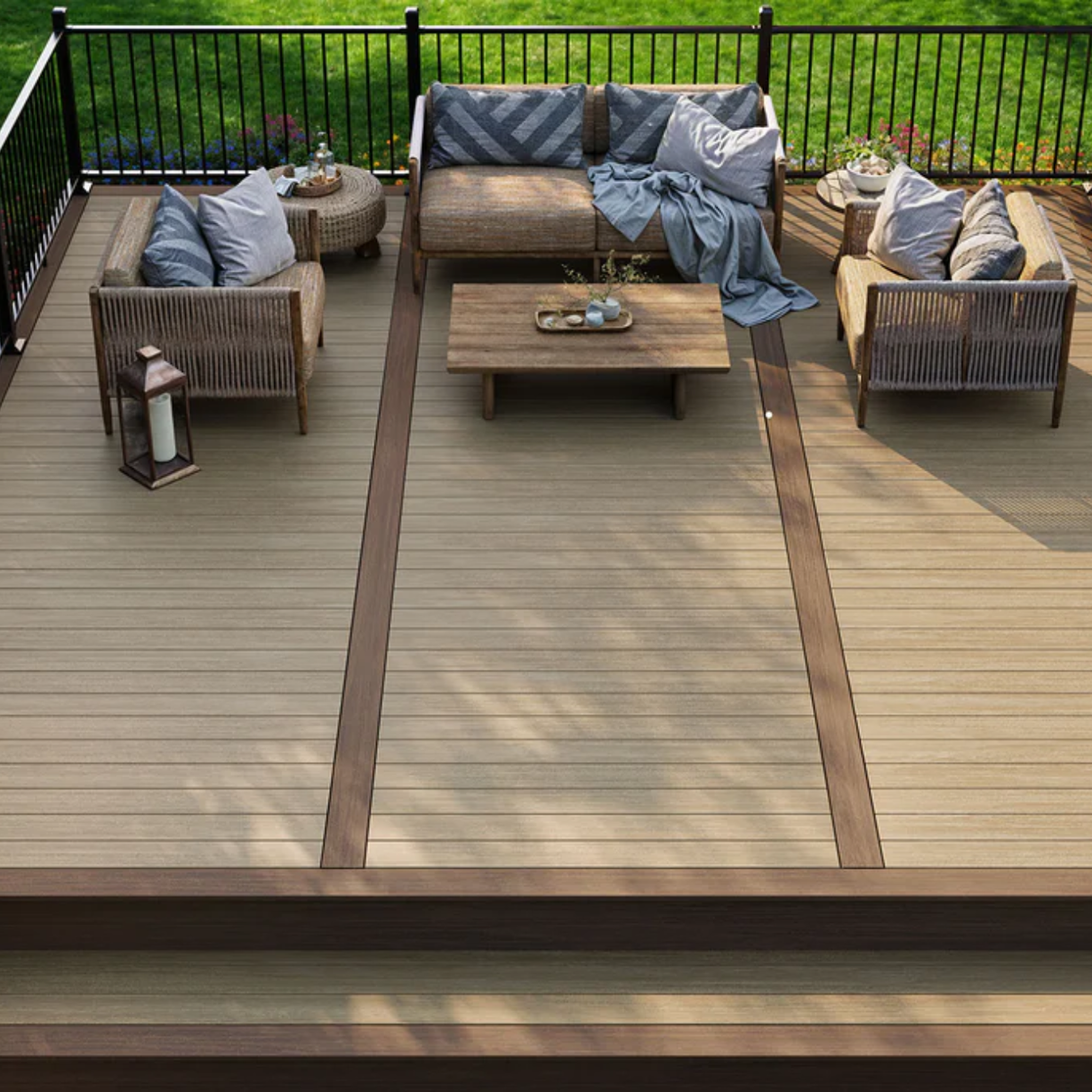 A modern two-tone composite deck featuring Deckorators Summit decking with a lighter field and dark brown border, furnished with stylish rattan outdoor seating and a black metal railing overlooking a green lawn.