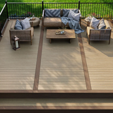 A modern two-tone composite deck featuring Deckorators Summit decking with a lighter field and dark brown border, furnished with stylish rattan outdoor seating and a black metal railing overlooking a green lawn.